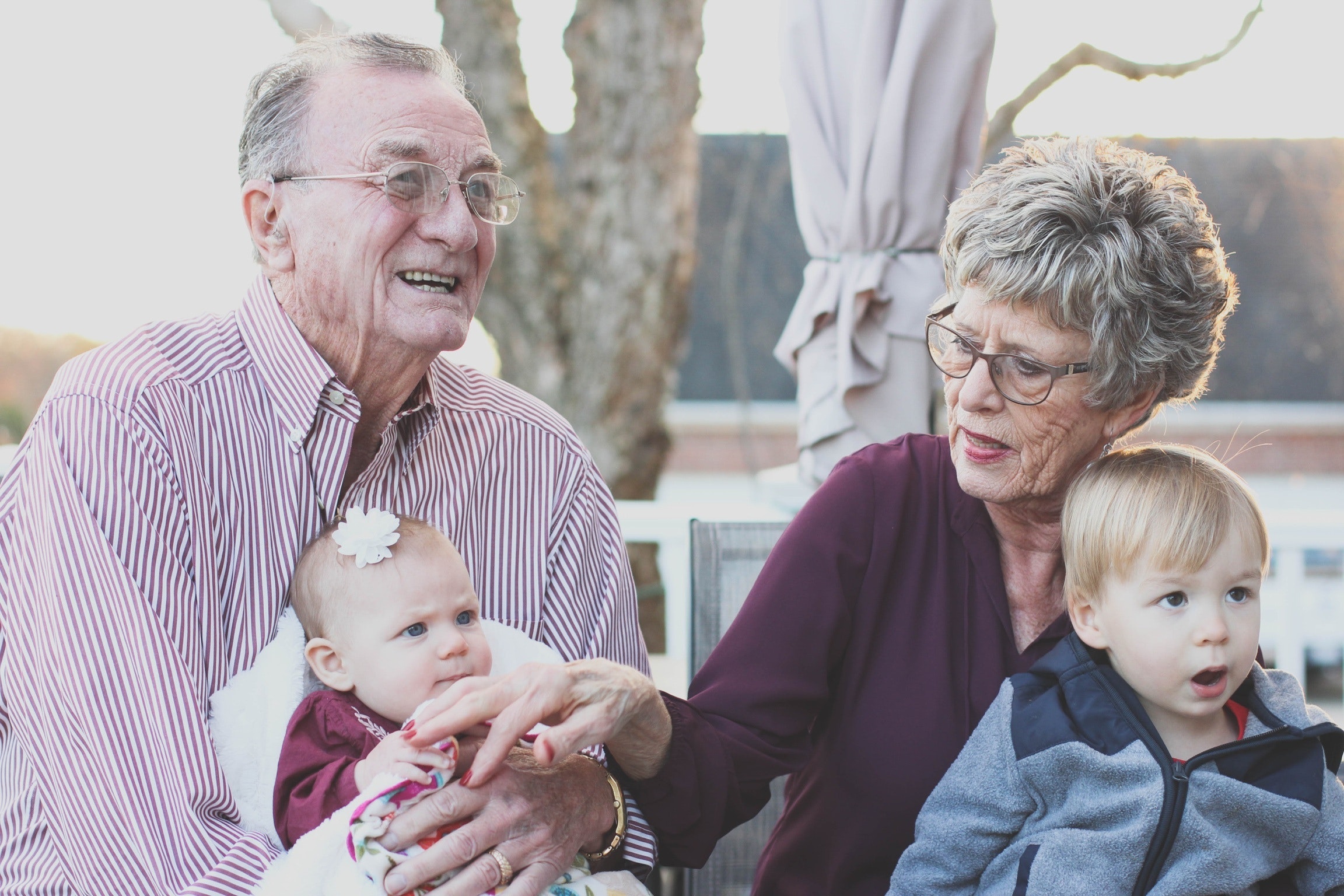 Older white man and woman sit outside with two young white children