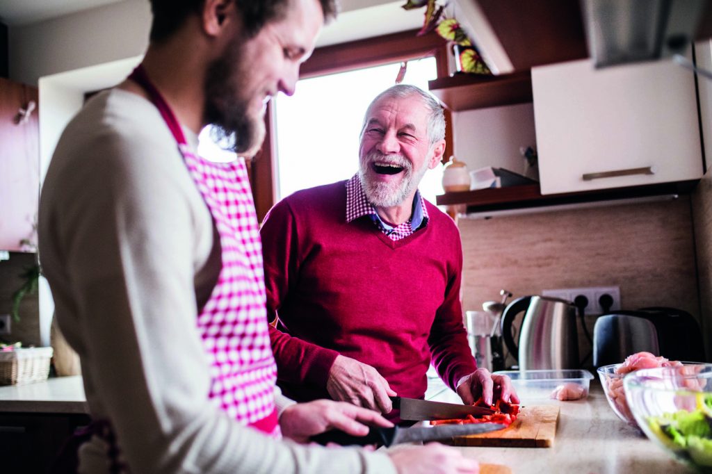An older white man smiles while cutting chillies with a younger white man.