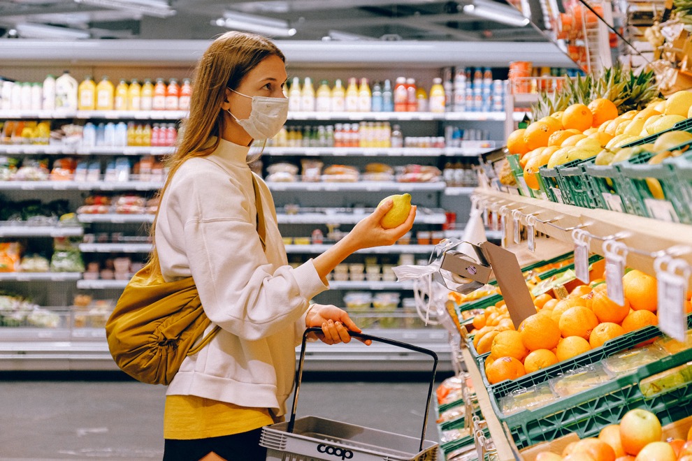 A woman wearing a protective face mask holds a piece of fruit in a supermarket. Photo by Anna Shvets from Pexels