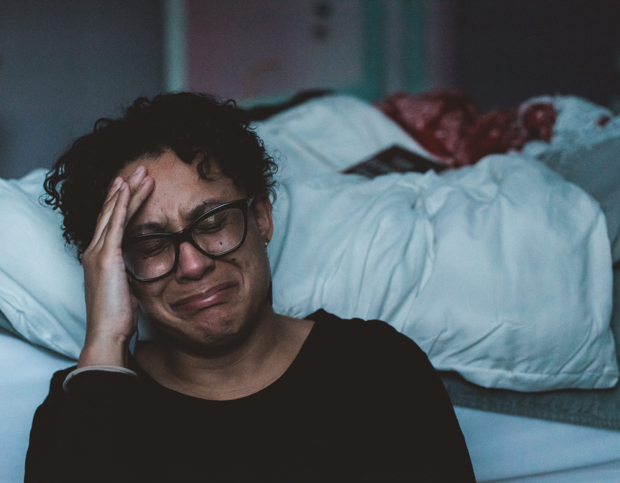 A woman cries by a bed side. Photo by Claudia Wolff on Unsplash.com